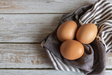 Brown chicken eggs lay on the wooden floor with brown fabric.