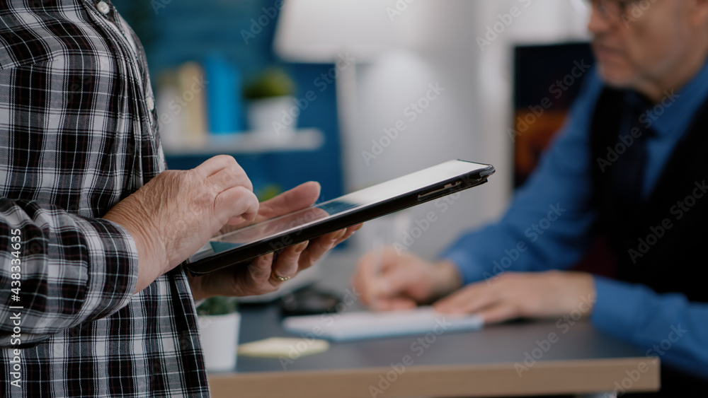 Poster close up of elderly woman employee texting, reading messages from tablet standing in home workspace 
