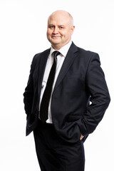 A smiling bald man in a strict black suit stands with his hands in his pockets. Business success. White background. Vertical.