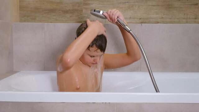 The boy holding shower head and washes his head in bathroom healthy childhood