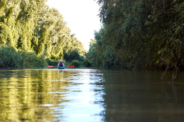 Woman row in blue kayak at wilderness areas of Danube river near green trees and thickets of wild grapes at spring