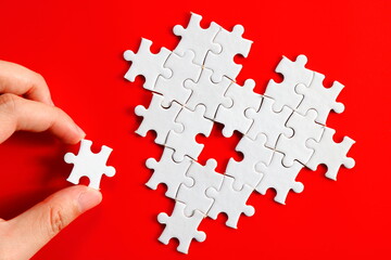 a hand fixing white jigsaw puzzle resemble incomplete heart love icon logo sign symbol in plain red...