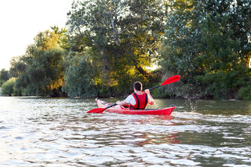 Man paddling in a red kayak on a Danube river at the sunset. Back view