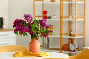 Vase with lilac flowers on table in kitchen
