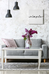 Cozy sofa and vase with lilac flowers near light wall