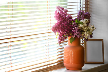 Vase with lilac flowers and blank frame on windowsill