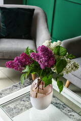 Vase with lilac flowers on table in room