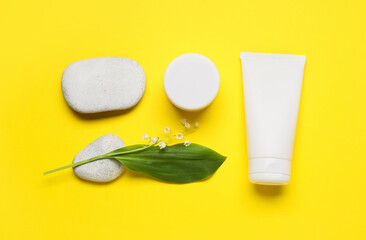 Cosmetic products, stones and lily-of-the-valley flowers on color background