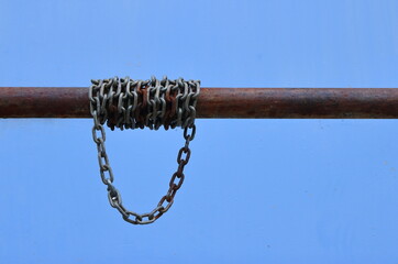 Closeup chain links wrapped around rusty pole against blue cement wall 