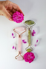Pink face roller and derma roller laying  on the flowers on white background. Beauty roller tools. 