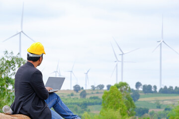 An engineer sits at his laptop looking at a clean energy wind turbine project to generate electricity.