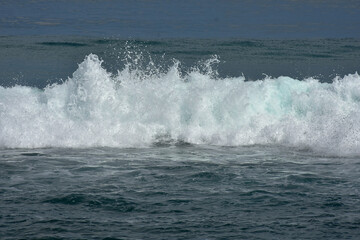 An ocean shorebreak in front view. Big beautiful green blue wave splashing with backwave and ready to break out. White foam sliding over sand. Bright sun shining on blue sky.