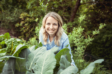 pretty young blonde woman with blue denim shirt works in garden at vegetable patch and is happy