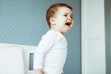 Boy baby crying in bedroom. Sad and angry child portrait