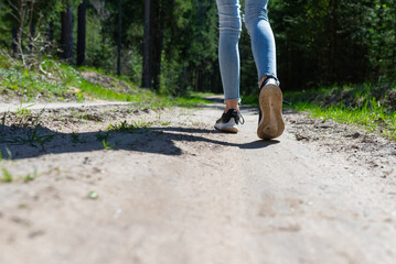 Rear view photo of female tourist legs walking in a forest road.Summer day.