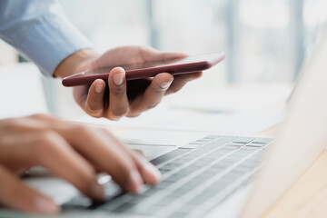 Businessman using smartphone and computer keyboard.