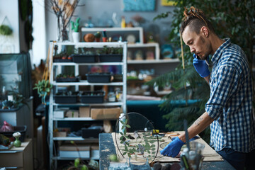 Bearded male herbalist talking on cellphone in workshop - obrazy, fototapety, plakaty