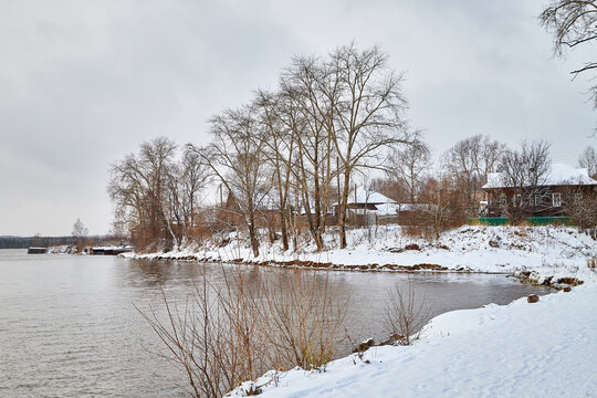 Nature landscape with wooden house in village on shore of lake with ice and snow in a cold winter or autumn day or evening