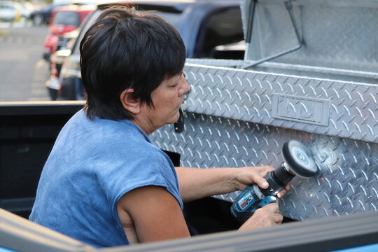 Woman Polishing Aluminum Toolbox With Power Tool While Sitting In Truck Bed