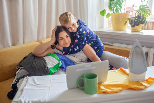 Middle aged mom and son talk to relatives via Internet while doing household chores, social media and gadget addiction, social distance and lockdown, new reality