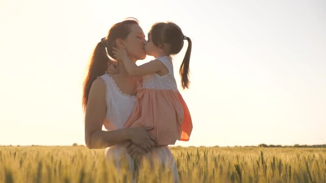 Happy family, Mom and little daughter are walking in yellow wheat field, hugging and kissing. Baby is in mom's arms. Farmer woman and child in field. A child and mom are walking in wheat field, travel