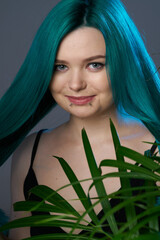 Naklejka premium Girl with blue green hair on a gray background, blue backlighting. Tropical plants around. Bright colored appearance of a creative person
