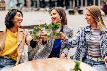 happy three friends young women sitting at the terrace cafe toasting with a cocktail. Young people lifestyle. selective focus on woman in the middle.