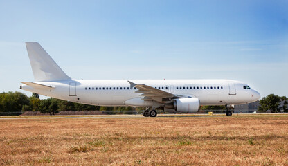 Fototapeta na wymiar A white plane on the airport runway is taxiing. Takeoff and landing. Arrival and departure. Place for text. Passenger plane mockup. Airplane flight. Travel by air transport. Copy space