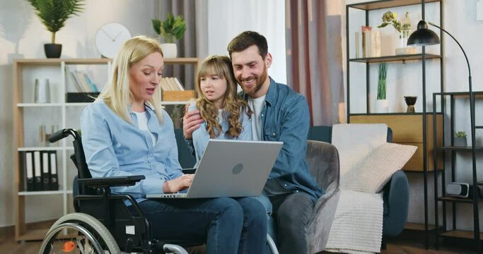 Family idyll of adorable joyful friendly loving family of daughter,father and disabled mother in wheelchair which together watching interesting program on computer at home