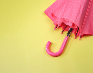 flat lay  of pink polka dot umbrella on yellow background. rainy season concept.