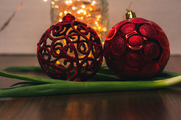 Two red Christmas balls, green onions and Christmas lights in a glass jar on a wooden table. Home decorations for the New Year 2022. Christmas background. Bokeh. Winter holidays