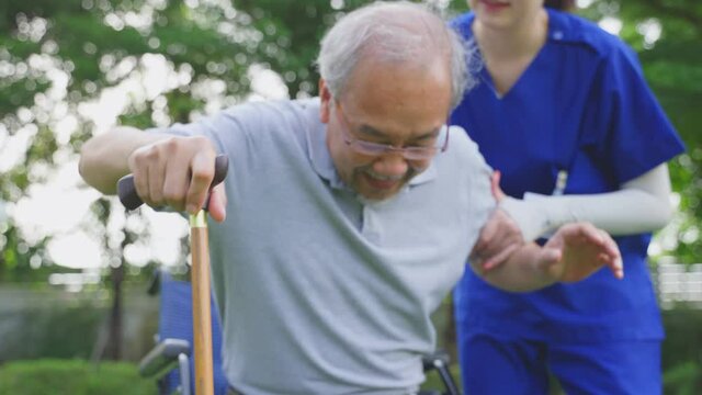 Asian old man practice walking in the public park by helping of nurse.	
