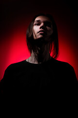 Fototapeta premium Portrait of a young man with long hair on a red and black background