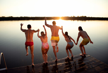 Young friends having fun enjoying a summer day swimming and jumping at the lake.