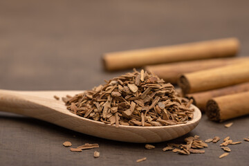 Wooden spoon with crushed cinnamon, rolls of cinnamon on a brown wooden background. Close-up, copy space.