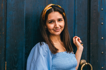 Fototapeta premium Young beautiful caucasian brunette woman portrait on a background of a blue door.