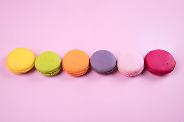 Lined up in a row of pastel-colored macaroons cookies on a pink paper background. Copy space