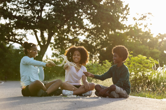 Young curly-haired African American teenger sitting on street and playing hay flowers at sunset time.