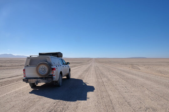 travel by camperized 4x4 car, white SUV in the middle of arid landscape and endless gravel road in namibia, africa