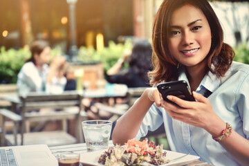 Asian woman smiling while playing on her phone in an outdoor cafe. face focus