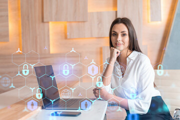 Attractive businesswoman in white shirt at workplace working with laptop to defend customer cyber security. Concept of clients information protection. Padlock hologram over office background.