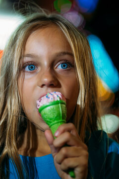 Little blonde girl eating a delicious ice cream in the amusement park