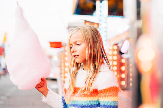 Little girl has fun at the fair with lights and eats sweet cotton.