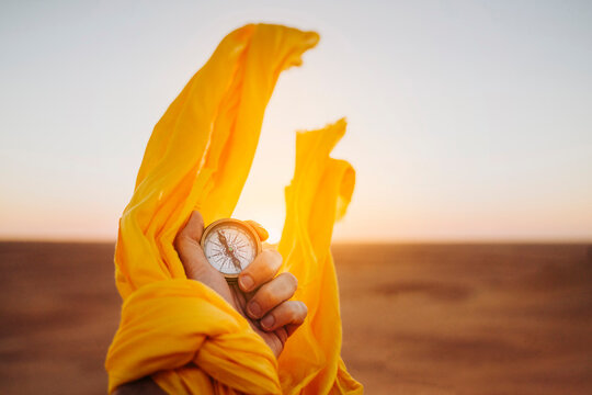 Hand holding a compass in the middle of the desert