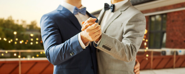 homosexuality, same-sex marriage and lgbt concept - close up of happy male gay couple holding hands and dancing on wedding over roof top party background