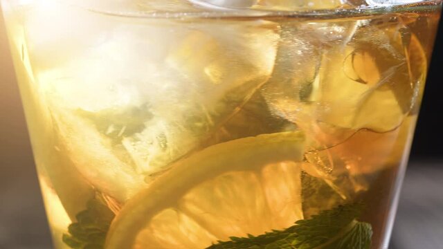 Closeup glass of iced tea with ice cubes, sliced lemon, fresh pepermint. Healthy refreshing lemonade for detoxification, sweet tasty soft drink or cold aromatic beverage for summer time in slow motion