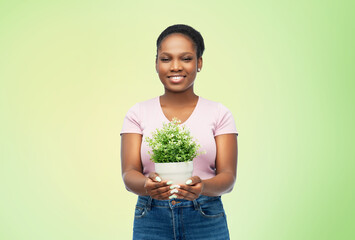 environment, nature and people concept - happy smiling african american woman holding flower in pot over green background