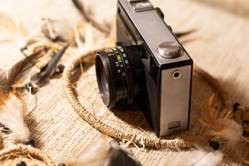 Old analog camera in front of beige background. The camera stands on the dream catcher, and...