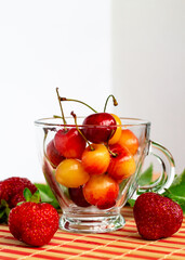 bright ripe yellow and red cherries in a glass cup with strawberries, healthy nutrition concept, summer organic fruit and berries