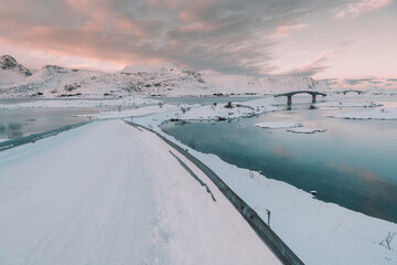 Road with bridges between water near mountain in snow